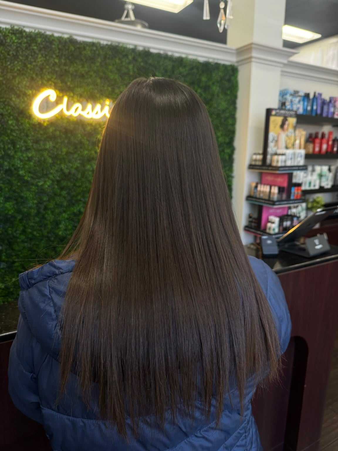 Woman with long straight brown hair in salon, "Classic" neon sign on green wall background.