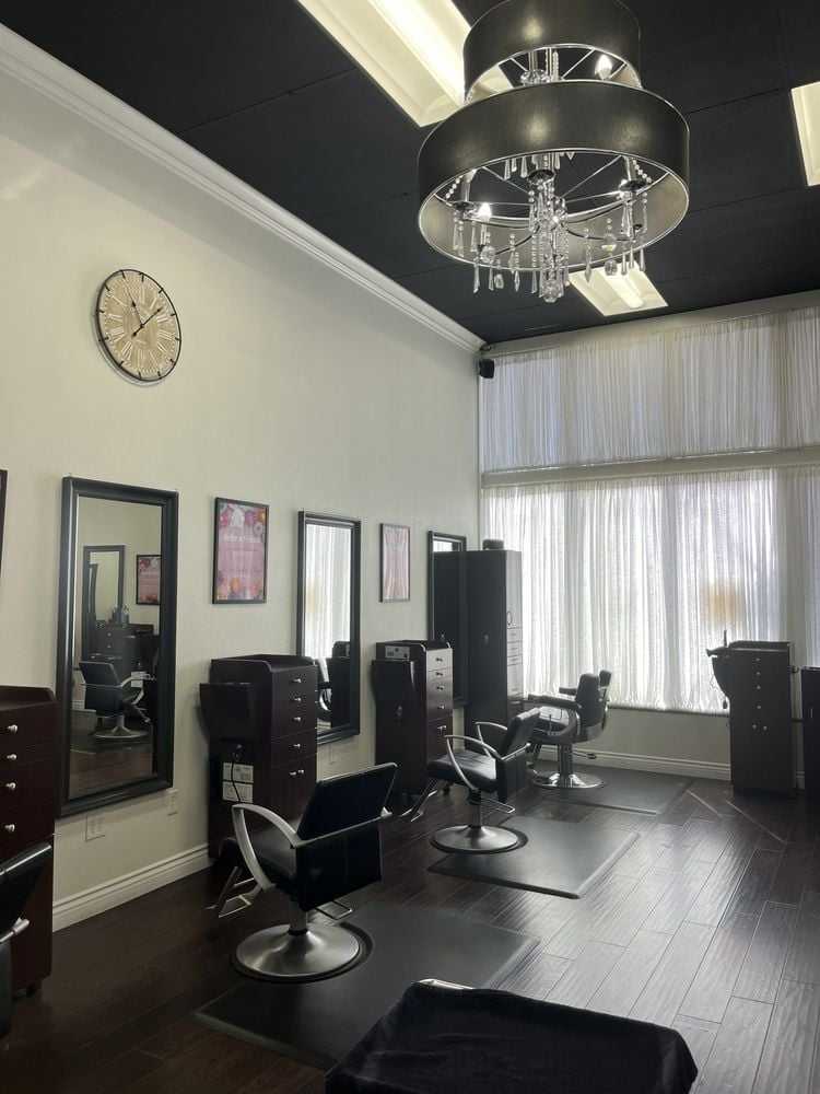 Elegant hair salon interior with stylish chairs, mirrors, chandelier, and modern decor.
